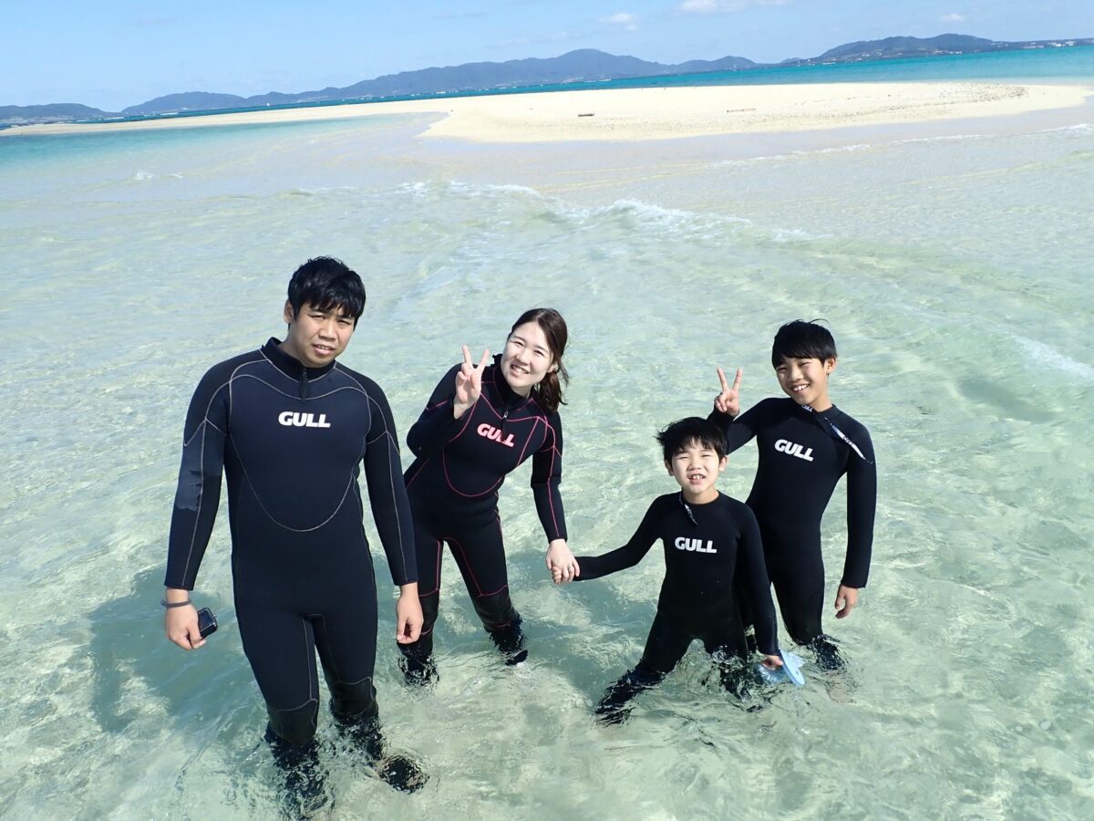 ウェットスーツを着て幻の島の浅瀬に立つ家族連れの参加者